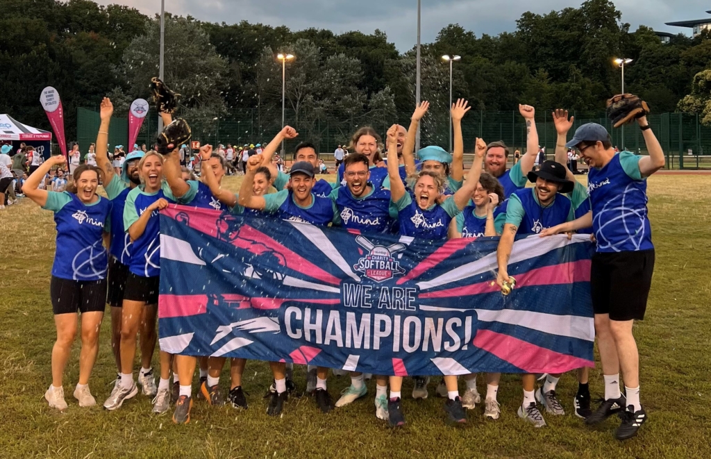 A group of the Mind charity team celebrating their win with a banner at the softball final